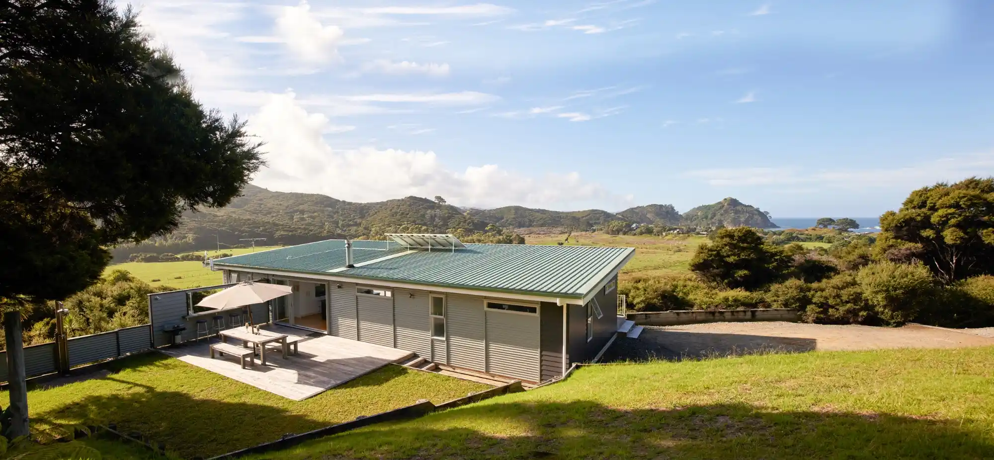 Ruru House and deck above native bush at Medlands Beach, Great Barrier Island