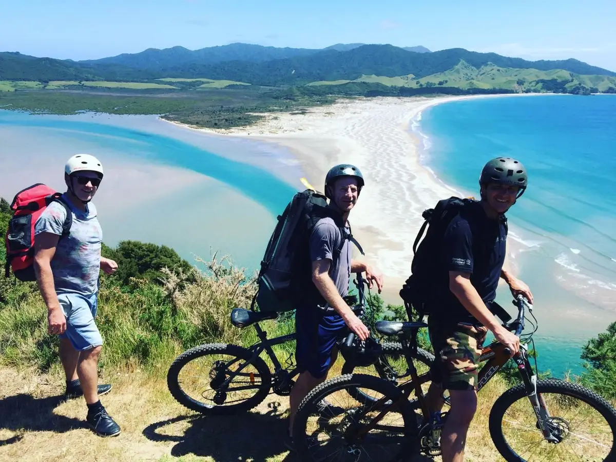 Three mountain bikers on the ridge above Whangapoua Beach, Great Barrier Island