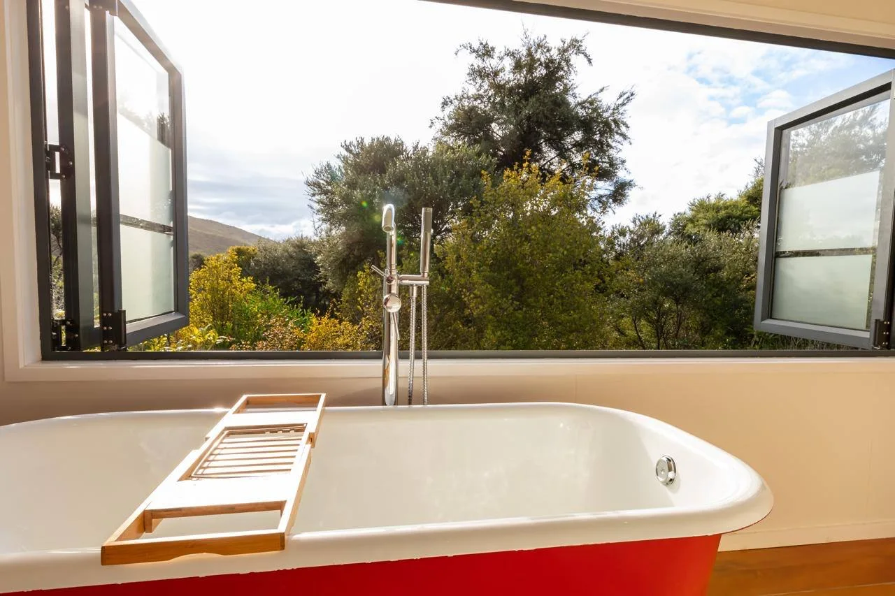 Red clawfoot bath with open window looking out to native bush, Tree House, Great Barrier Island
